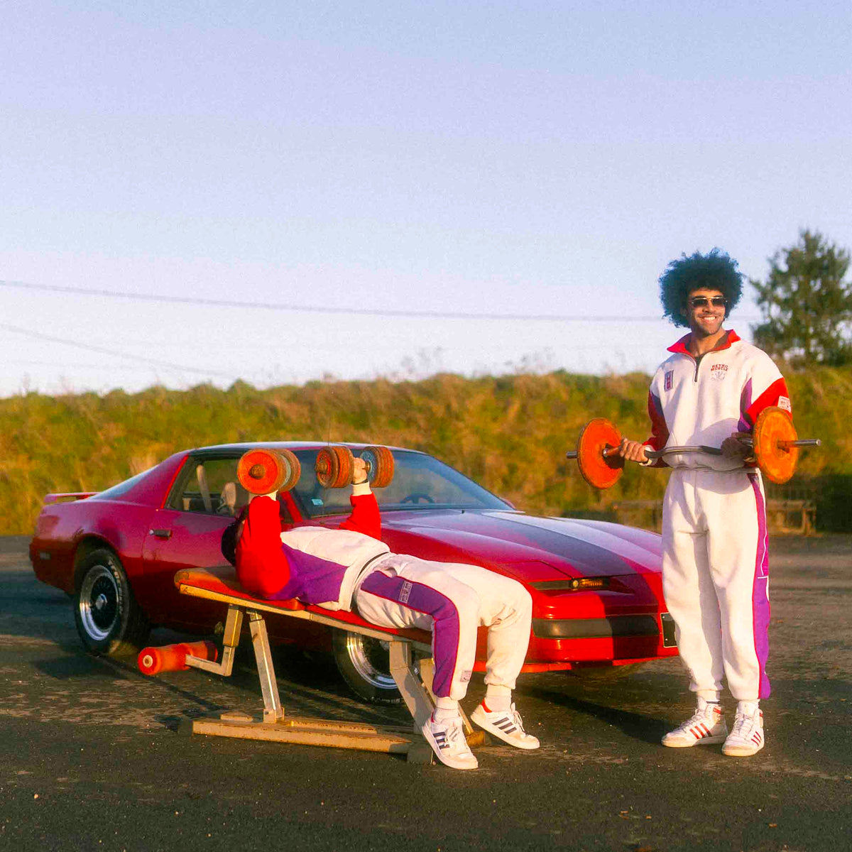 deux athlètes année 80 avec des joggings vintages devant une pontiac firebird